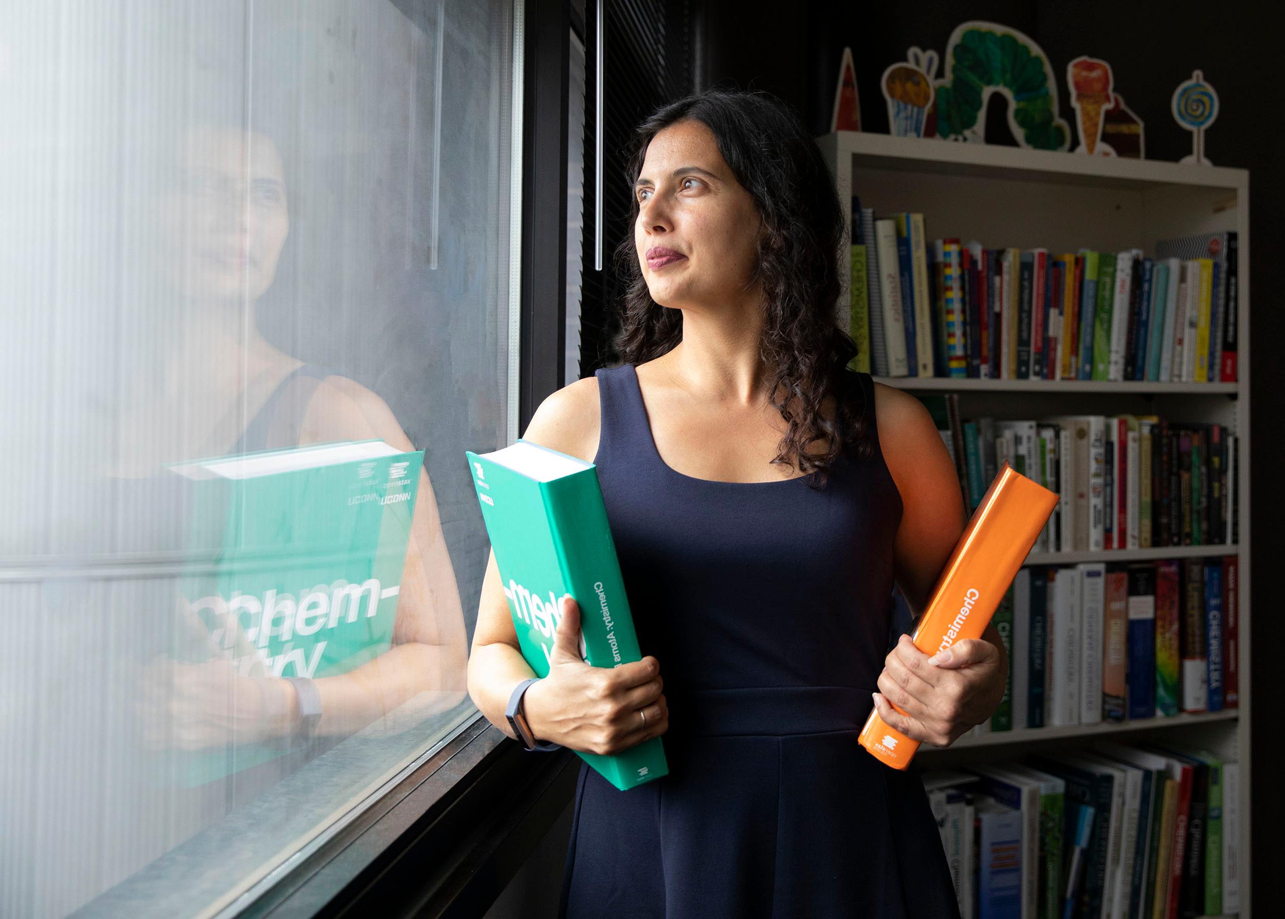 Emily Ragan looking out a window holding two books in each arm