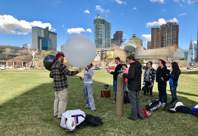 Students preparing to launch a weather balloon from a campus greenspace