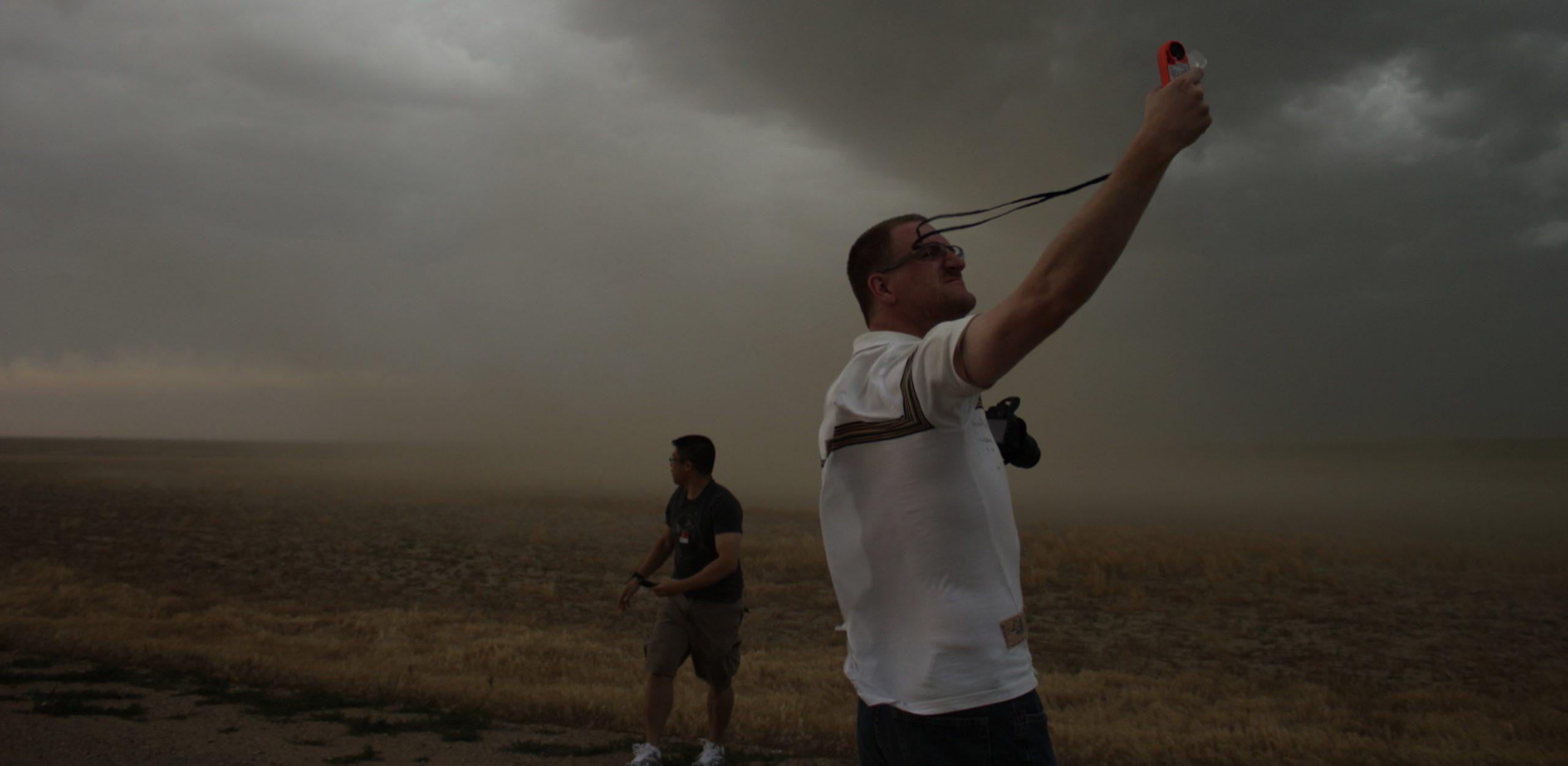 A student holds out a meteorological instrument to measure the wind during a gusty severe storm event