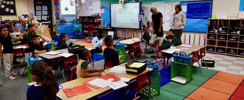 Photograph of two teachers instructing children in a classroom.