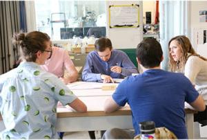 Industrial Design students talking and sketching around a lab table.