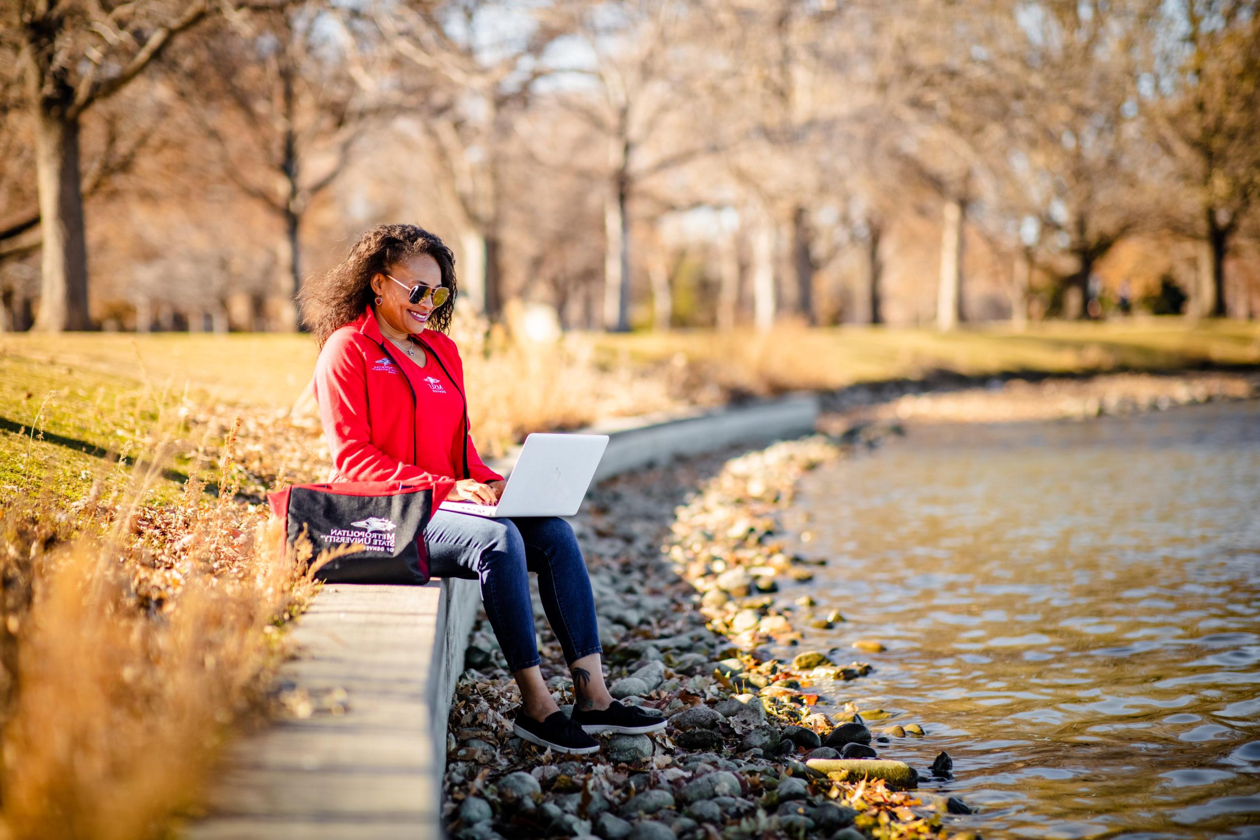 A student sitting on a concrete seat outside typing on their laptop