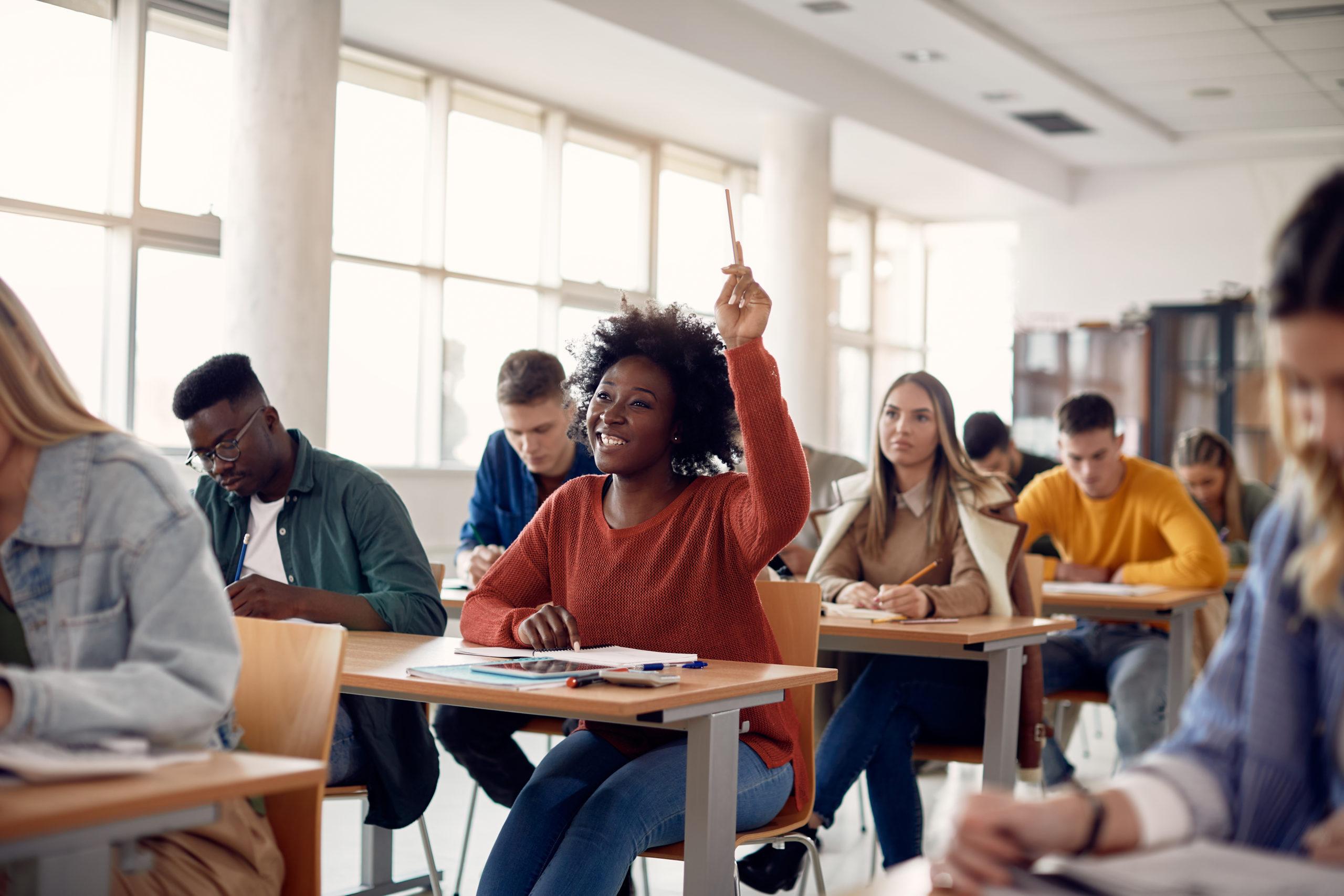 Happy African American student raising her hand to ask a question during lecture in the classroom.