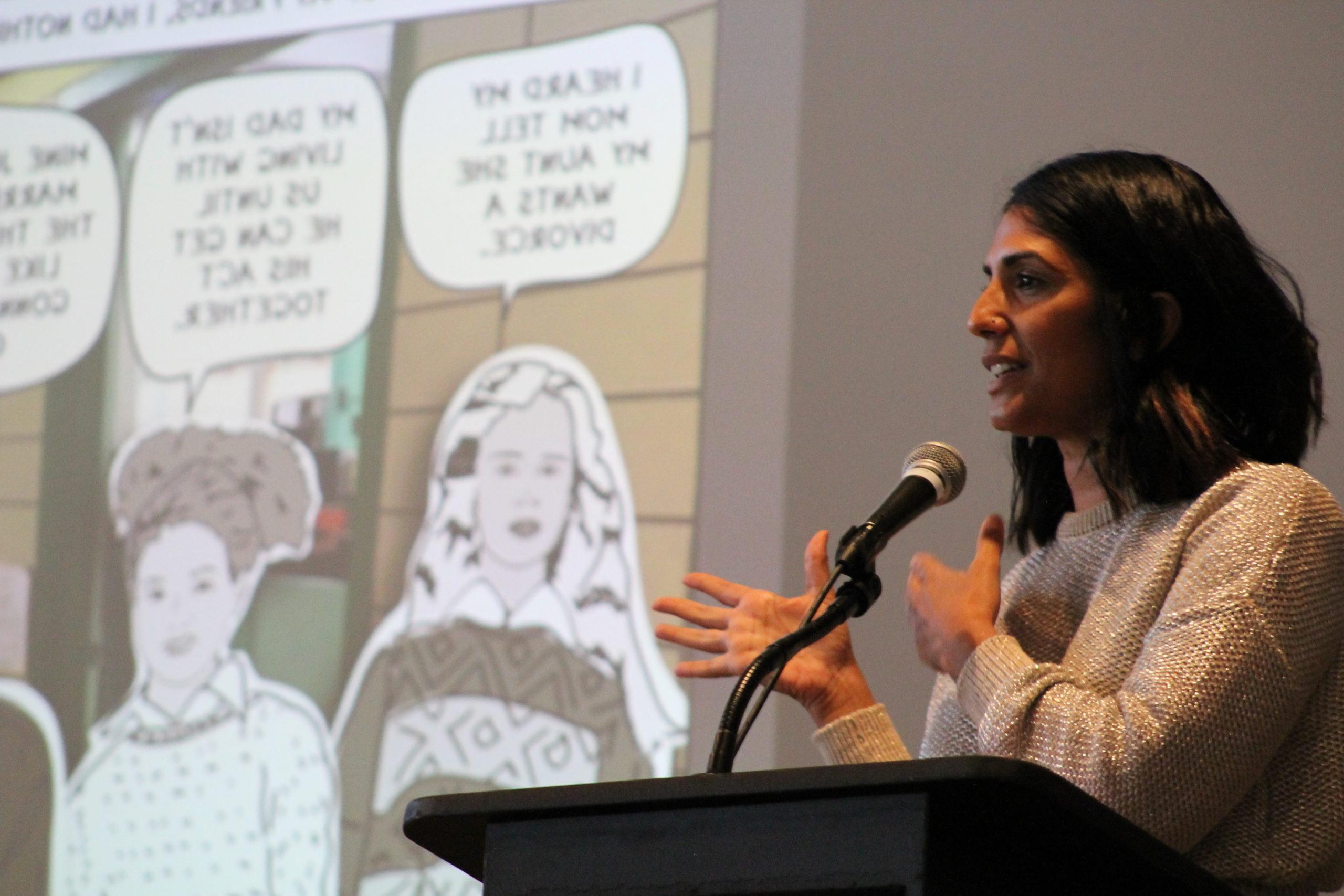 Mira Jacob speaks to the audience with her book displayed on the projector behind her.