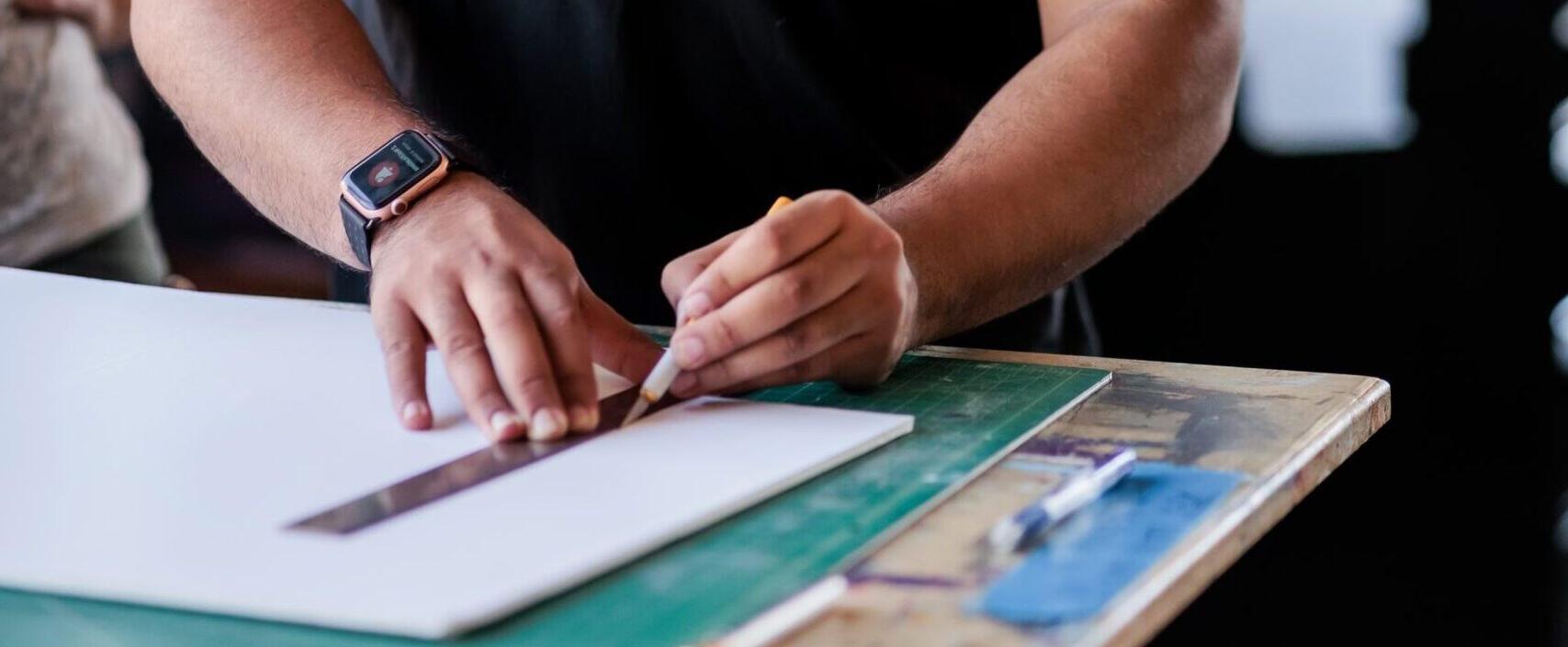 Student at a desk measuring with a ruler to cute a white sheet of paper