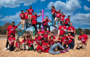 A photo of one of the MSU Denver MISTERs sitting with a group of young students and holding two books.