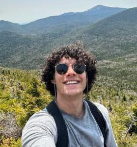 Lukas M in front of a green and mountainous landscape.