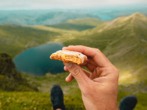 close up of someone holding up a snack with their feet mountains and lakes in the background