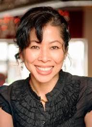 Headshot of Luong Ung, wearing a black shirt with ruffles and black styled hair that is slightly curled