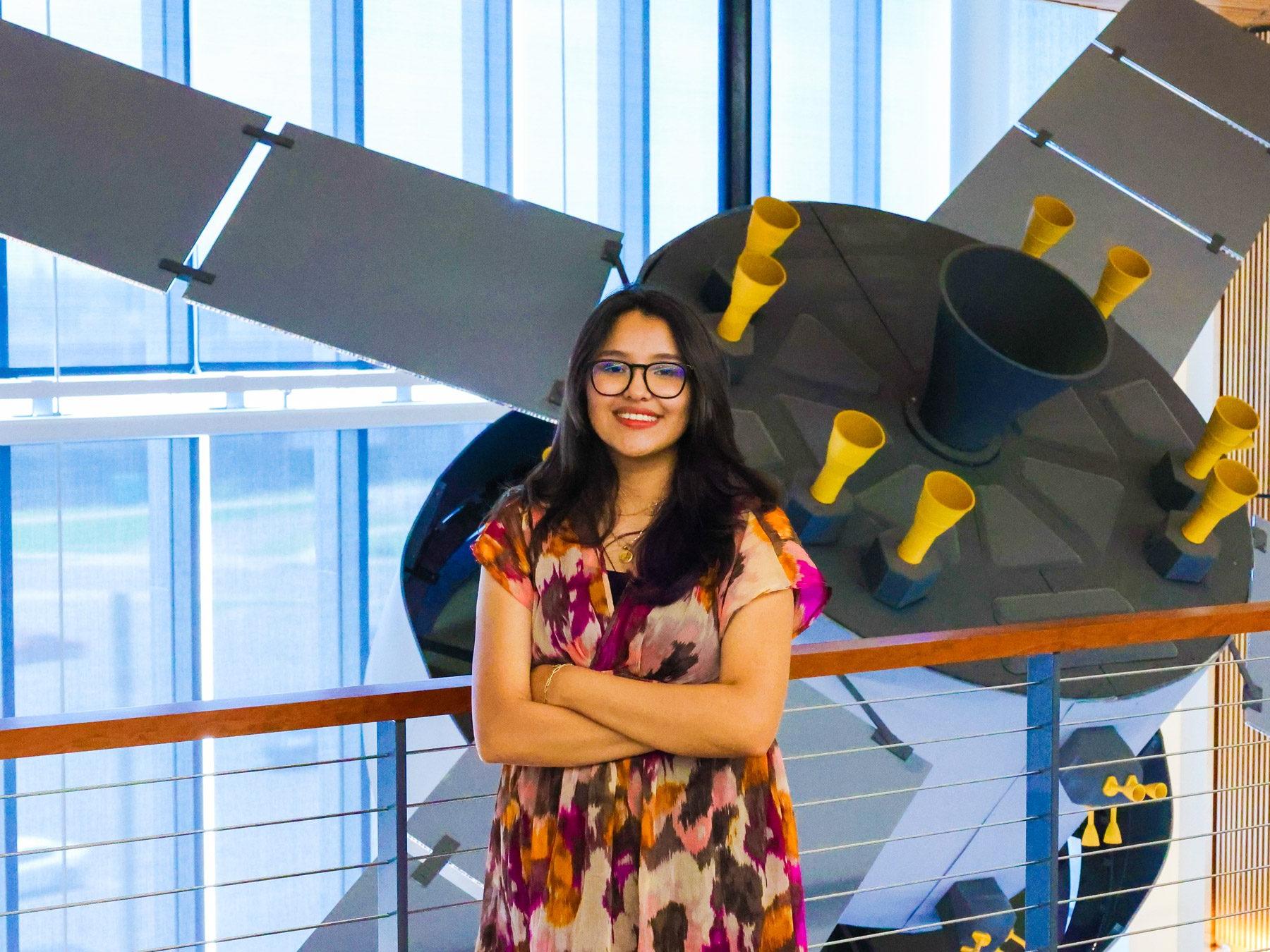 Aerospace engineering technology major Evelyn Montes Gonzalez standing in front of the satellite in the AES building