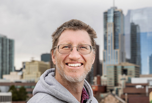 Dr. John Carter smiling with the Denver skyline behind him