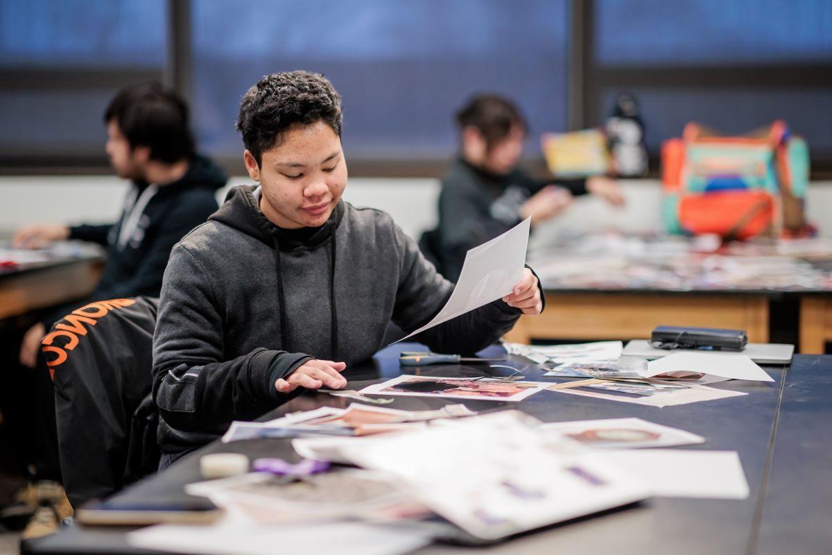 A student smiles as they hold a piece of paper while working on a project